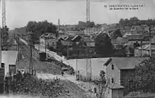 Vue prise en hauteur à proximité du tunnel avec, au premier plan, la ligne, le passage de la route de Nantes et la maison du garde barrière, à droite, la ville et, en arrière-plan à gauche, la gare