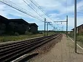 Au premier plan, 2 voies ferrées et un aiguillage les reliant, en arrière plan, un hangar de stockage avec du foin rempli à ras bord.