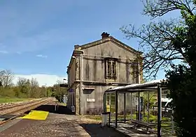 Photo des voies et quais avec le bâtiment voyageurs d'origine et l'abri de quai de la halte.