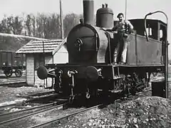 Photo noir et blanc d'une petite locomotive à vapeur vue de face et son chauffeur.