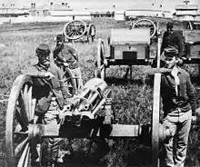 Photographie noir et blanc de quatre soldats dont les deux situés en avant-plan sont appuyés sur les roues d'une mitrailleuse.