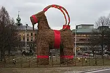 bouc en paille orné de tissu rouge, au milieu d’une pelouse