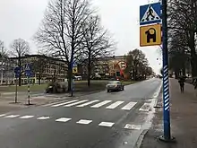 passage piéton ; à côté se situe un poteau avec un panneau représentant la silhouette du bouc en noir sur fond jaune.