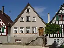 Maison à étage, au toit pointu, rosée, vue de face, dans un groupe de trois maisons similaires