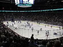 vue en plongée sur un stade de hockey durant une compétition. Les joueurs d'une équipe sont habillés en rouge et blanc, les autres en bleu