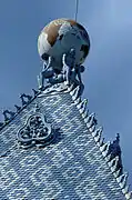 Couverture en tuiles vernissées et ornements en céramique bleue de Zsolnay. Au sommet de l'édifice, quatre silhouettes humaines ploient sous le poids du monde
