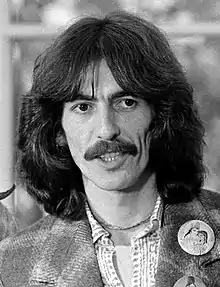 Photographie en noir et blanc d'un homme aux cheveux longs bruns portant la moustache, regardant vers sa gauche.