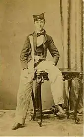 Photographie jaunie montrant un jeune homme à casquette négligemment assis sur une table.