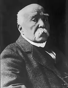 Photographie en noir et blanc de Clemenceau, sur fond noir, buste tourné vers la droite, tête regardant l'objectif légèrement en contrebas, avec un air impérieux.