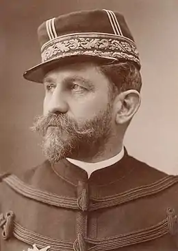 Photo en noir et blanc et de trois-quarts d’un homme en tenue de militaire, cheveux foncés, épaisses moustache et barbe commençant à blanchir, portant une médaille sur le côté droit de la poitrine