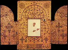 Photo d'un objet en or en trois parties, au centre une image de femme dont on voit que le visage et les mains
