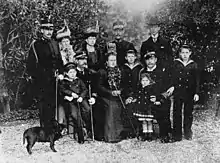 Photographie en noir et blanc d'un groupe de douze personnes d'âges et de sexes différents et d'un chien.