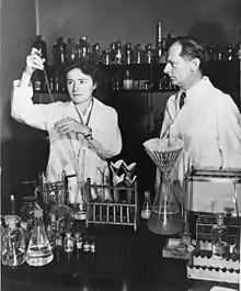 Photographie en noir et blanc montrant un homme et une femme en blouses dans un laboratoire.