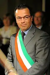 Photographie d'un homme ceint d'une écharpe comprenant trois bandes aux couleurs du drapeau italien.