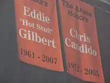 Deux bannières orange suspendu au plafond d'une salle. Sur celle de gauche est écrit Eddie Gilbert et sur la seconde Chris Candido.