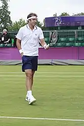 Photo d'un joueur de tennis gaucher qui est en train de demander une balle à un ramasseur situé hors champ