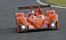Phographie d'une voiture orange, vue de face, sur une piste.