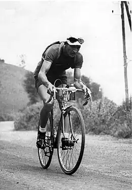 Photographie en noir et blanc d'un cycliste courbé sur son vélo, pédalant dans la montée d'un col.