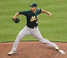 Un joueur de baseball habillé d'un T-shirt vert foncé et d'un pantalon gris en train de lancer une balle.