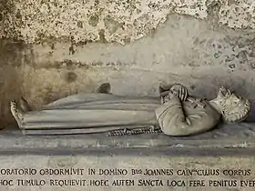 Photographie en couleurs d'une statue de gisant au fond d'une niche dans un mur.