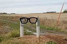 Une sculpture représentant deux poteaux blancs tenant une monture de lunettes noires comme celles de Buddy Holly.