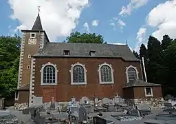 Édifice religieux en brique de style néo-roman. Au premier plan, un cimetière, en arrière plan, une forêt.