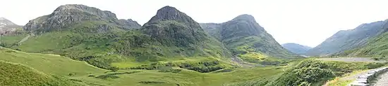 Vue panoramique sur de hautes collines verdoyantes, sous le soleil.