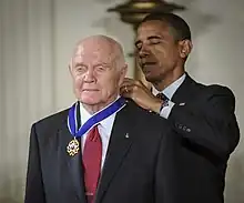 Barack Obama remettant la Médaille de la liberté à Glenn par derrière.