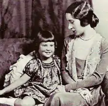 Photographie en noir et blanc d'une petite fille souriante assise à côté d'une femme qui la regarde.