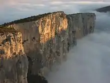 Photographie montrant une falaise vue du haut entourée de nuages