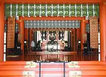 Photo couleur de l'intérieur du bâtiment du culte d'un sanctuaire shintō (couleur dominante : orange).