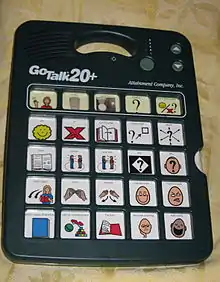 Système électronique de communication vocale avec haut-parleurs, comportant une fente pour insérer différentes cartes. Ici, la carte comporte 25 symboles issus d'un livret de lecture.
