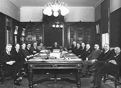 Photographie noir et blanc de quatorze hommes assis autour d'une table.