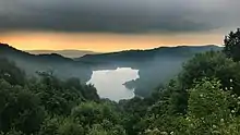 Par dessus la canopée, un lac brille dans une légère brume.