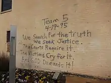 Les inscriptions suivantes sont écrites sur un mur : Team 5 ; 4-19-95 ; We search For the truth ; We seek Justice ; The Courts Require it ; The Victims Cry for it ; And GOD Demands it !.