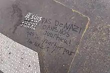 Sur le bitume, un graffiti "Je suis Alain Soral" réalisé avec un pochoir. Le nom d'Alain Soral est barré au marqueur par une personne ayant écrit à côté "Pas de nazi dans nos quartiers ! Pas de quartier pour les nazis !".