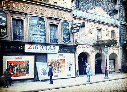 Durant la Grande Guerre, en 1917 ou 1918, des badauds (dont un soldat en uniforme bleu horizon) contemplent des affiches annonçant la ressortie de deux films Zigomar d'avant-guerre au « Grand Cinéma Plaisir » sis au 95 bis, rue de la Roquette à Paris 11e. Autochrome d'Auguste Léon,.