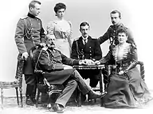 Photographie en noir et blanc montrant quatre hommes en uniforme et deux femmes autour d'une table.
