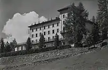 Photo noir et blanc d'un grand bâtiment blanc caché derrière une rangée de pins.