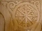 Photographie d'une inscription coufique rayonnante, inscrite dans un cercle orné de fleurons. Elle est située à gauche de la niche du mihrab.
