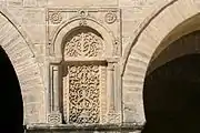 Photographie d'un panneau sculpté de la façade du portique occidental de la cour. Ce panneau en pierre est orné d'un décor symétrique de rinceaux et de fleurs, se terminant par un croissant.