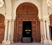 Photographie montrant la porte la plus grande et la plus ornée de la salle de prière. Renouvelée en 1828-1829, sa décoration est composée de motifs géométriques et végétaux, de moulures, ainsi que d'inscriptions en relief.