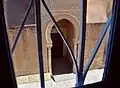 Vue du porche de Bab al-Ma depuis une fenêtre grillagée. Il est ouvert par un arc outrepassé brisé.