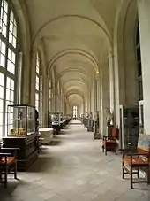 Longue galerie voûtée avec grandes fenêtres à gauche et mobilier