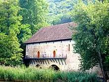 Photographie couleur d'un bâtiment médiéval en pierres situé non loin de la rive d'un lac, dont il est séparé par des roseaux