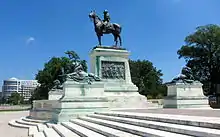 Photographie d'une statue équestre en bronze située sur un piédestal en marbre. Ce dernier est entouré de quatre statues de lions allongés également en bronze.