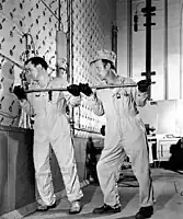 Ouvriers utilisant une tige pour pousser des barres d’uranium dans la face de chargement en béton du réacteur au graphite X-10.