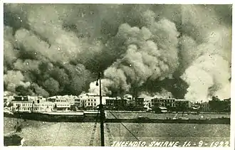 Photographie en noir et blanc montrant d'immenses volutes de fumée sur les bâtiments d'une ville.