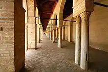 Vue intérieure du portique oriental avec, au milieu, une rangée d'arcades à colonnes de remploi. Il est couvert d'un plafond en bois à solives apparentes.