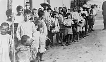 Photographie en noir et blanc montrant une foule d'enfants en guenilles formant une file.